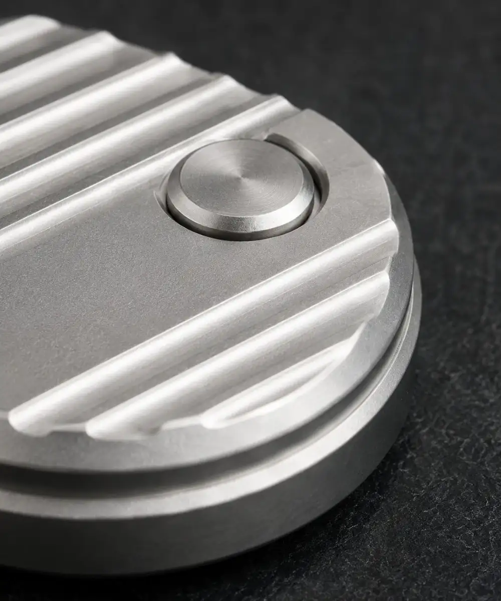 Close-up of an aluminum EDC fidget tool showing a light silver machined surface and rounded detail.